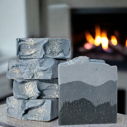 Five bars of soap sit in front of a fireplace. The soap has three layers of charcoal gray, with the darkest on the bottom and lightest at the top.