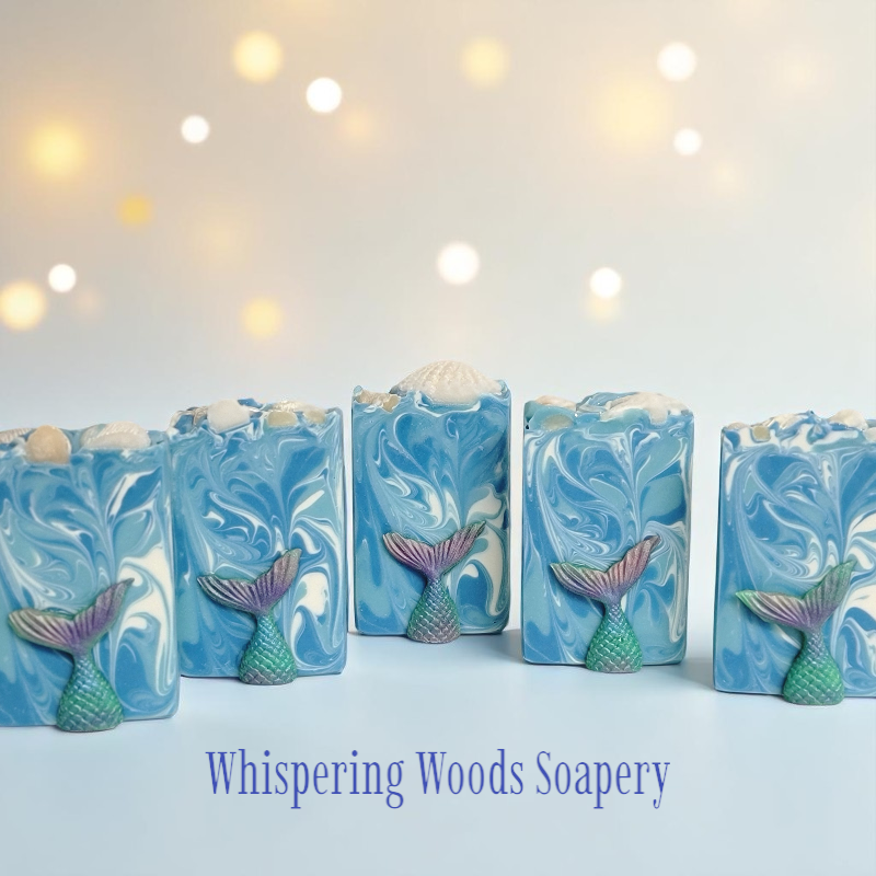 Five bars with blue and white swirls on a soft-lit background. Each bar of soap has a small mermaid tail in hues of teal, turquoise, pink and purple affixed to the front.