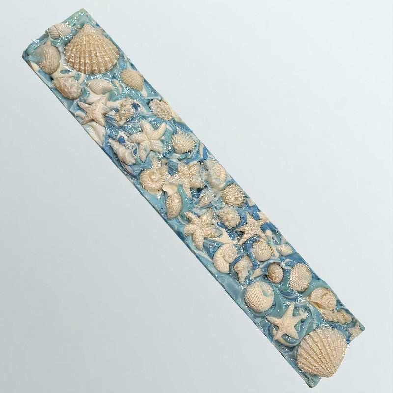 A loaf of soap with pearly white seashells sits on a light blue surface