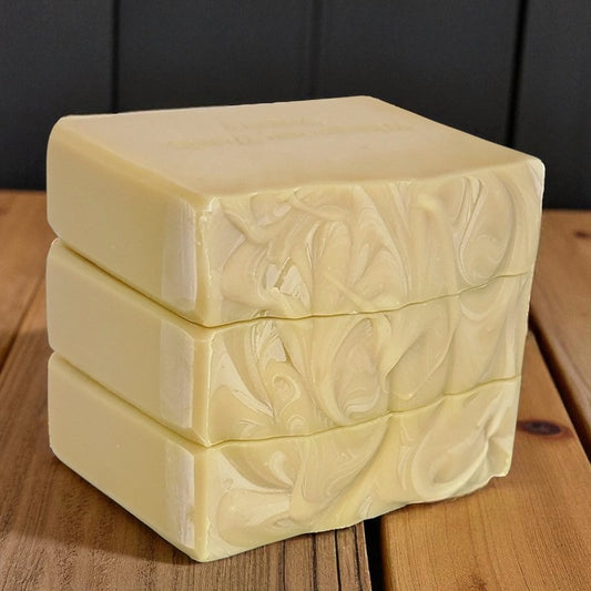 Three pale yellow bars of soap stacked on a wood surface