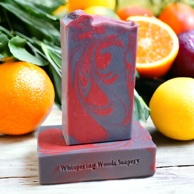 Two gray and red bars of soap with lemons and oranges behind them