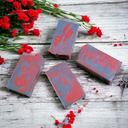 Four red and gray soaps lay flat on a light gray wood surface, with small red flowers scattered about