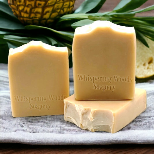 Three bars of yellowish-tan soap on a table with a pineapple in the background