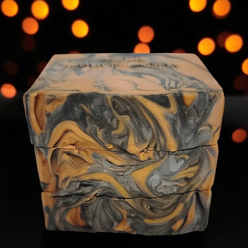 Marbled soap bar tops with orange and gray swirls on a dark background with blurred lights