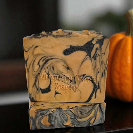 Marbled orange and black soap bars with 'Whispering Woods Soapery' branding next to a pumpkin