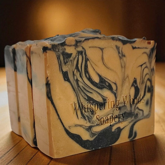 Marbled orange and black soap bars with 'Whispering Woods Soapery' branding on a wooden surface
