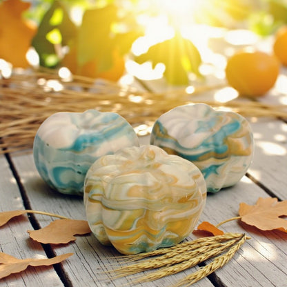 Teal, cream and orange swirled pumpkin soaps on a wooden surface with autumn leaves and sunlight in background