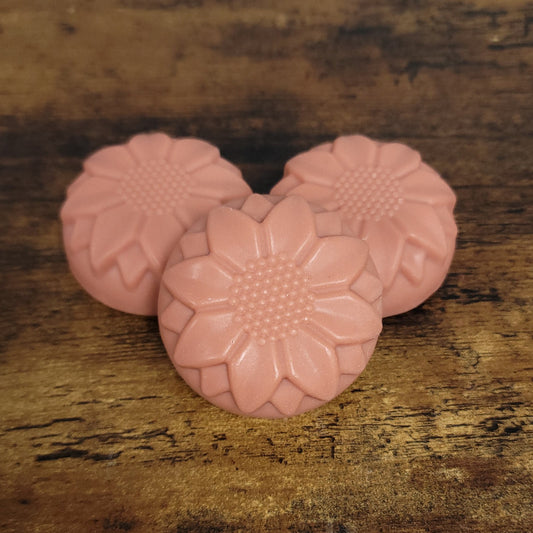 Three rose-clay-colored flower facial soaps on a wooden surface