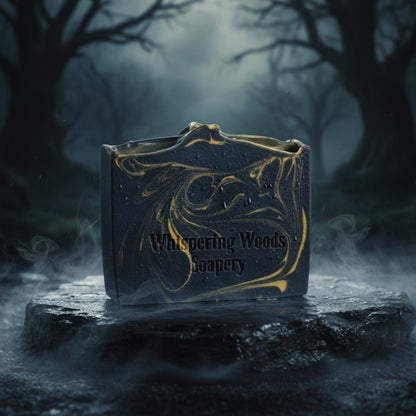 Bar of black soap with gold swirls, with 'Whispering Woods' branding, in a dark forest setting