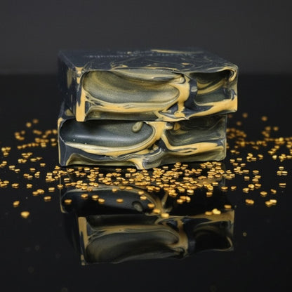 Marbled black and gold soap bars with gold glitter sprinkled on a reflective surface