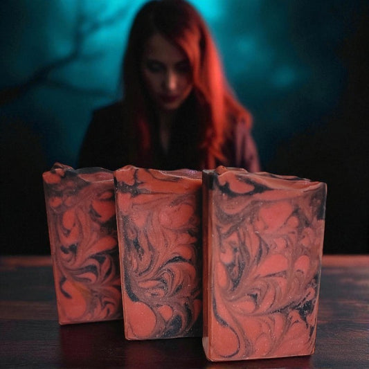 Three marbled soap bars of red and black on a dark surface with a blurred  redheaded woman in the background