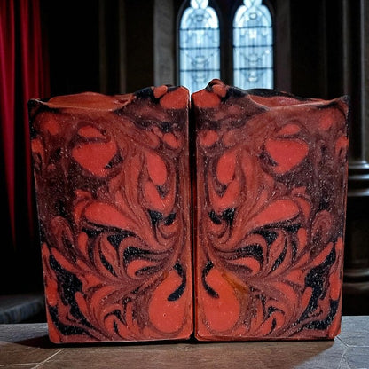 Decorative soap bars with intricate red and black design on a dark surface with gothic windows behind them