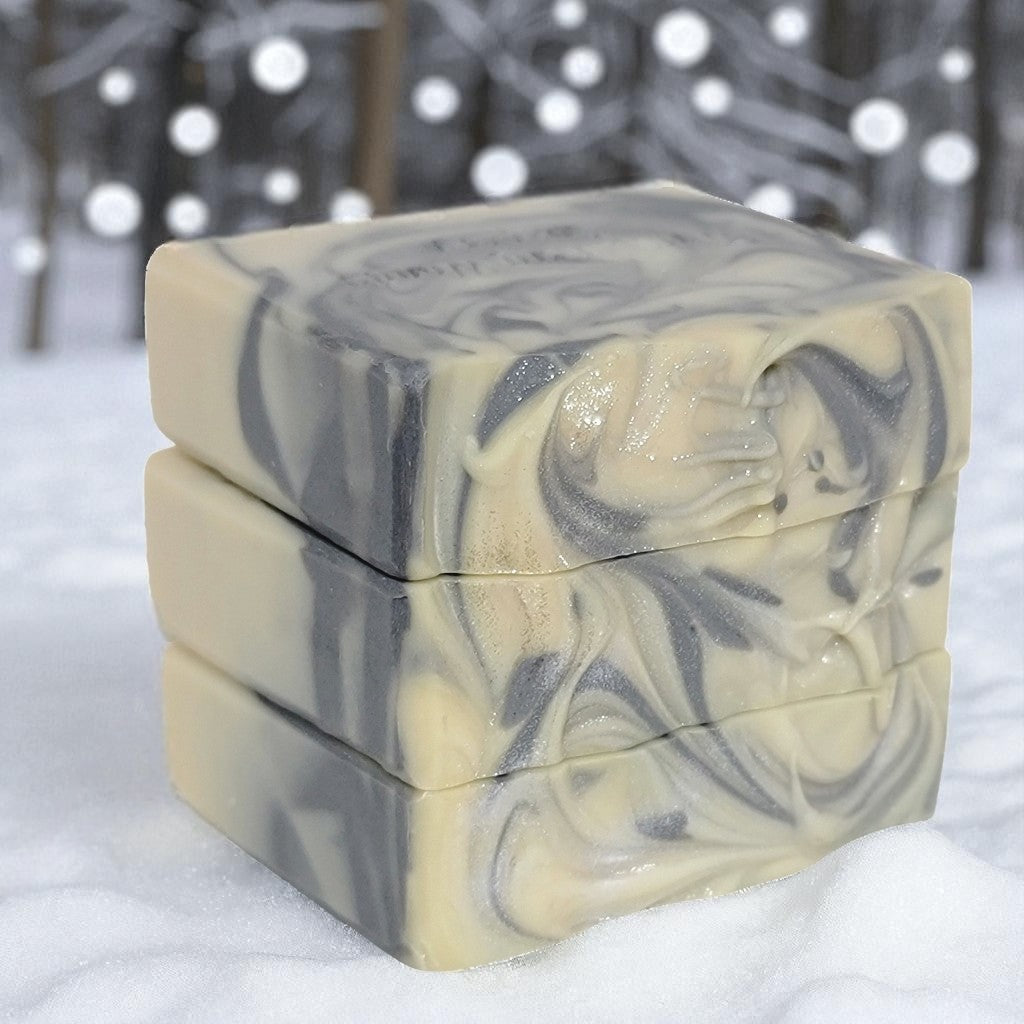 Three stacked bars of white soap with a silver swirl sitting atop snow