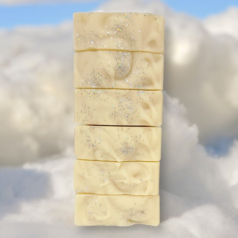 Six bars of pale yellow soap with silver sparkles on top stacked on each other with clouds in the background