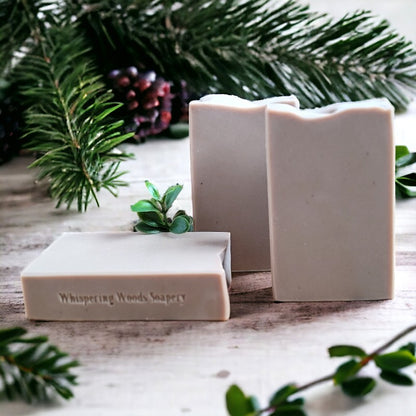 Three light brown bars of soap on a wood surface with pine branches in the background