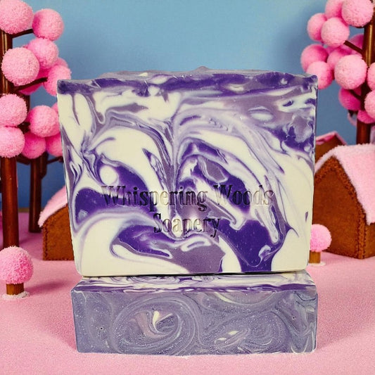 Marbled purple and white soap with 'Whispering Woods Soapery' branding on a pink surface with decorative elements