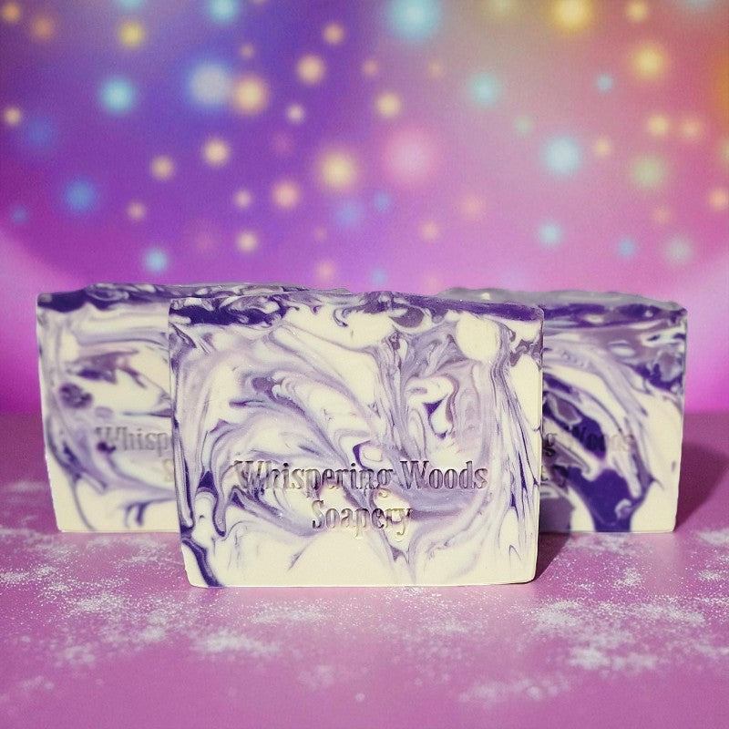Purple and white marbled soap bars with 'Whispering Woods Soapery' branding on a colorful pinkish background