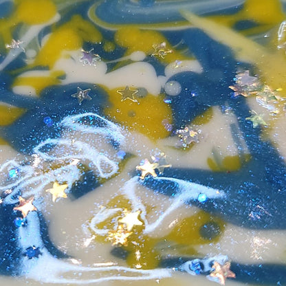 Extreme close-up of the top of wet soap colored white, yellow and blue with star glitter