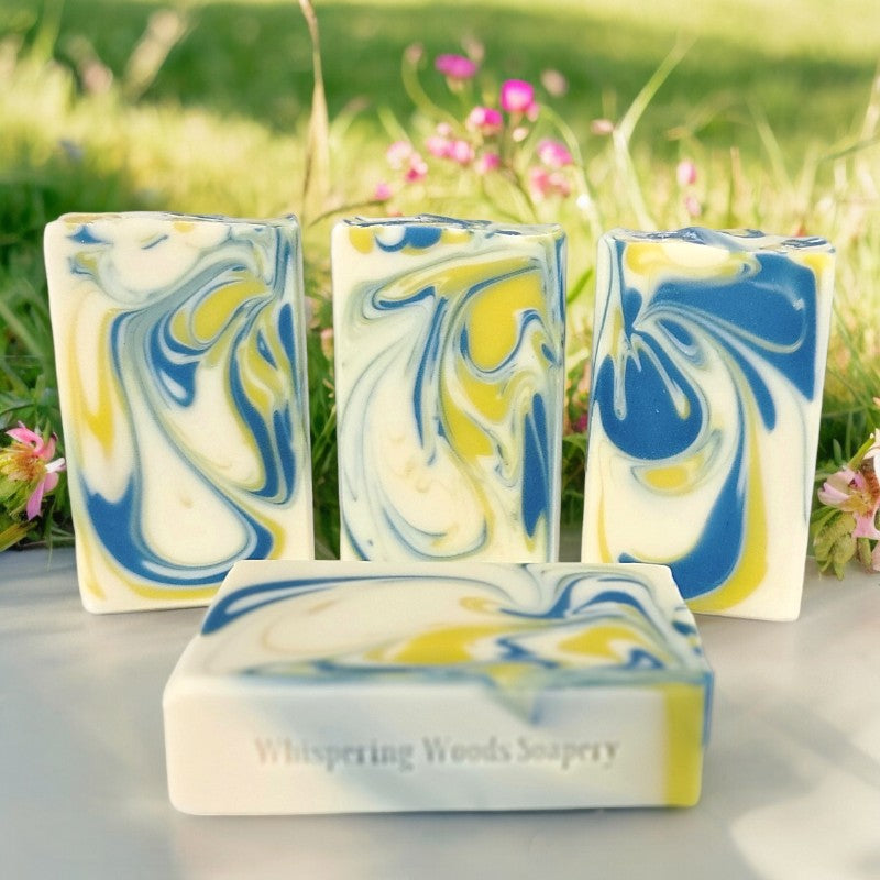 Four bars of white soap with yellow and blue swirls on a white surface with a spring meadow in the background