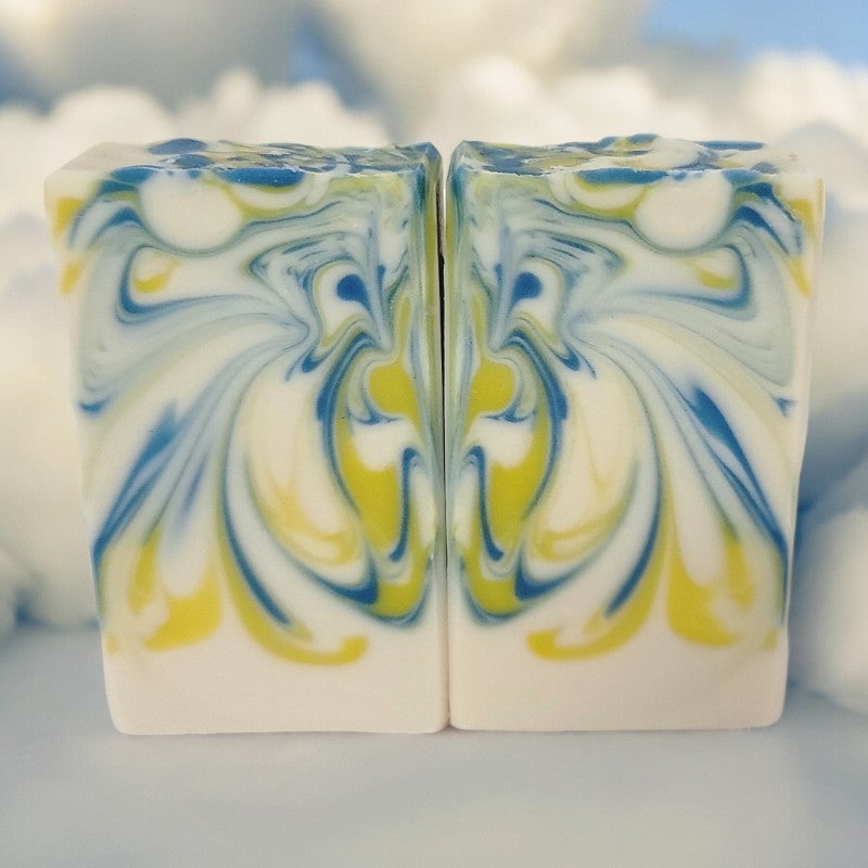 Two bars of white soap with yellow and blue swirls with clouds in the background