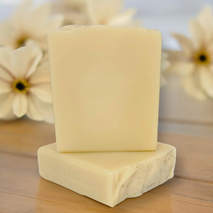 Two bars of pale yellow soap on a wood surface with white flowers in the background