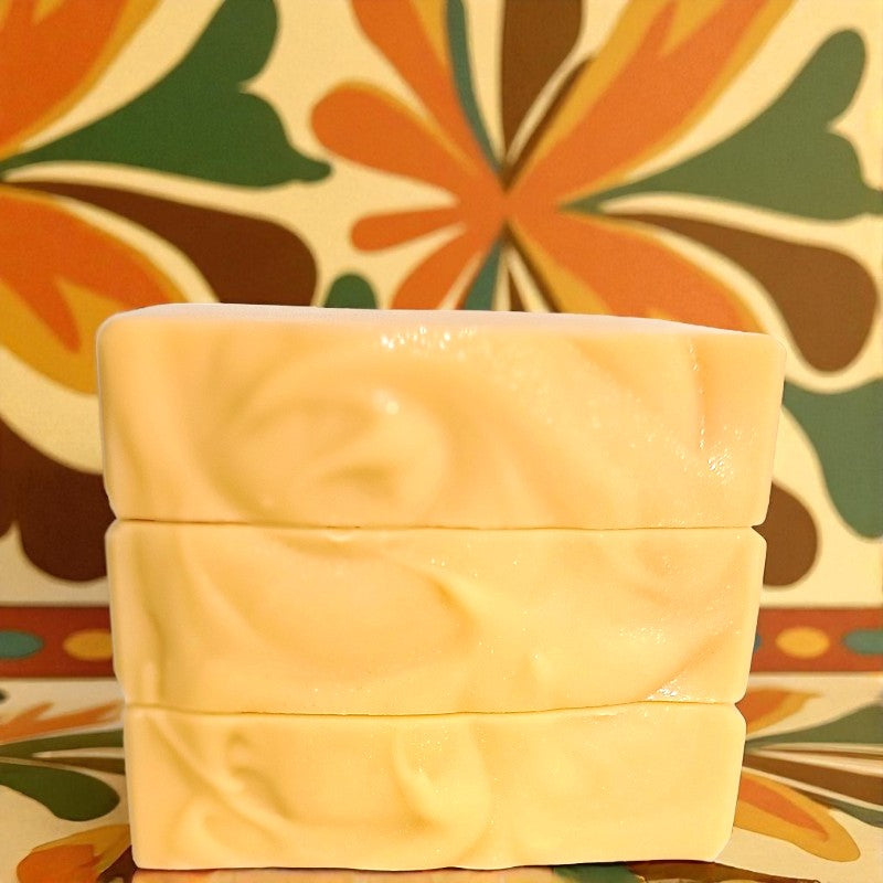 Three stacked bars of light orange soap with a colorful floral pattern wallpaper in the background