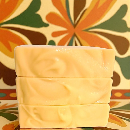 Three stacked bars of light orange soap with a colorful floral pattern wallpaper in the background