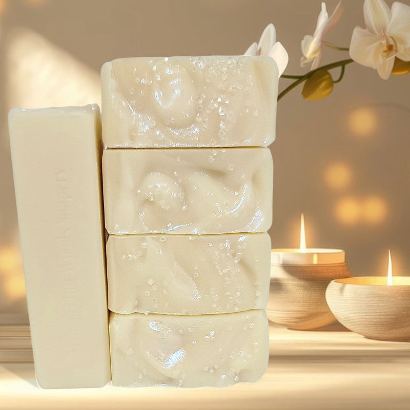 Five cream-colored soap bars stacked on a wood table with an orchid and candles beside them