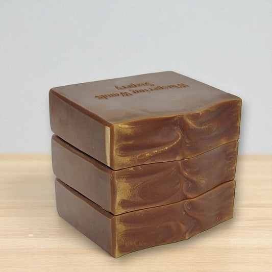 Three stacked bars of brown soap on a light wooden surface with a light gray background