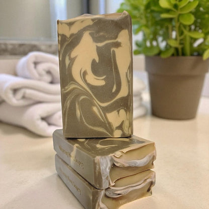 Stack of marbled soap bars on a surface with a plant and towel in the background