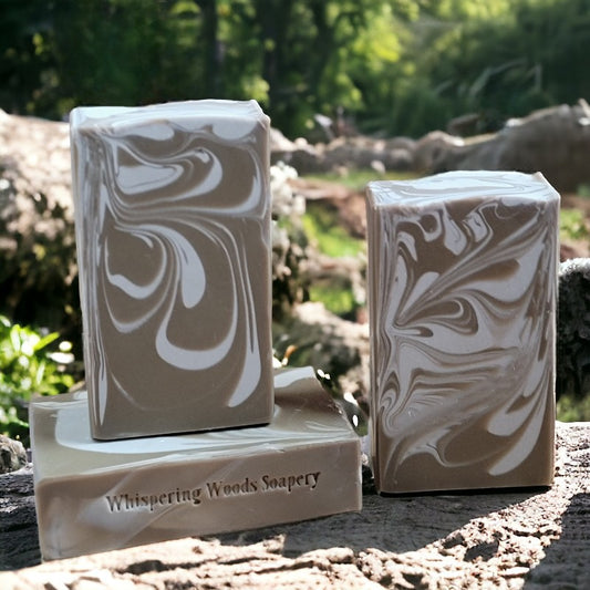 Three bars of soap with light brown and cream swirls on a stump with the woods in the background