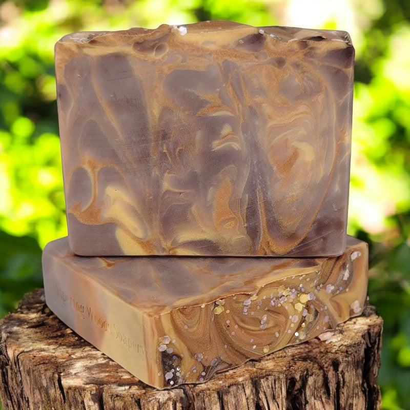 Two brown, gold and copper soap bars on a stump in a sun-dappled woods