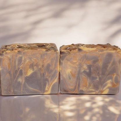 Two brown, gold and copper soap bars on sun-dappled concrete