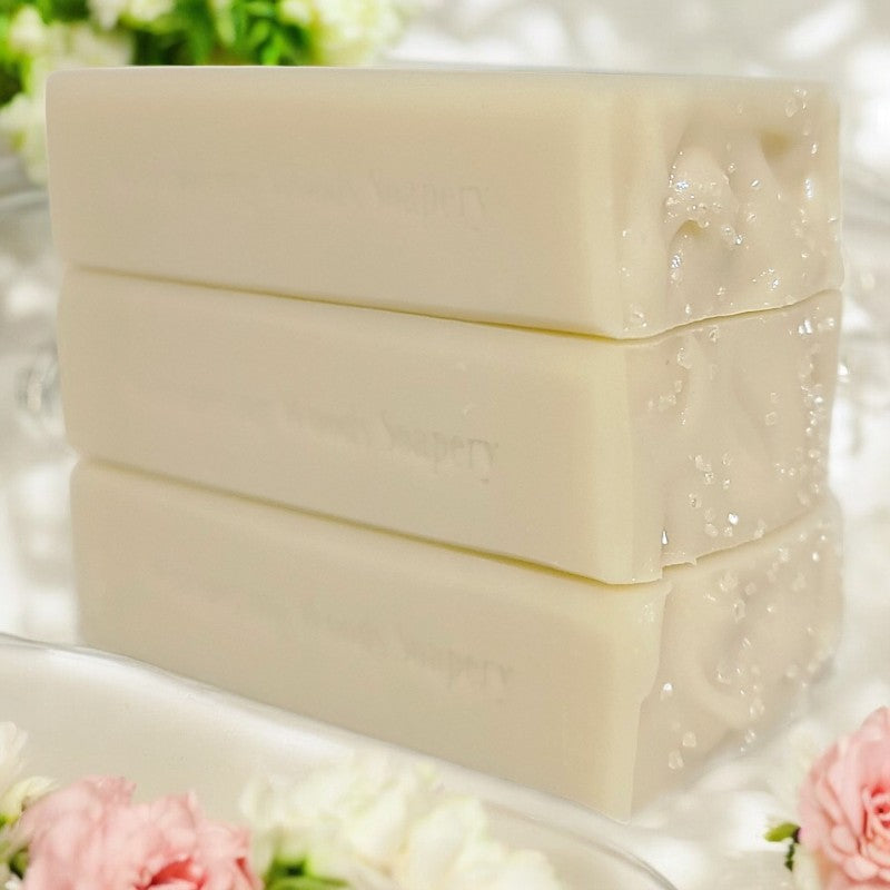 Three cream-colored soap bars stacked on a bathroom counter with cream and pink flowers around them