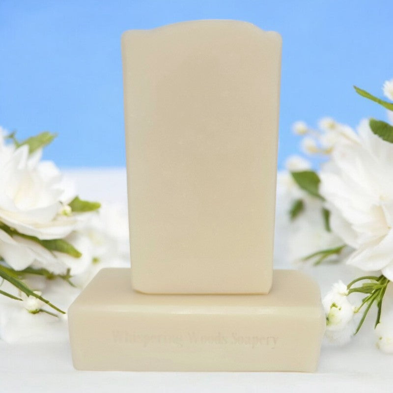 Two cream-colored soap bars on a white surface with white flowers surrounding them