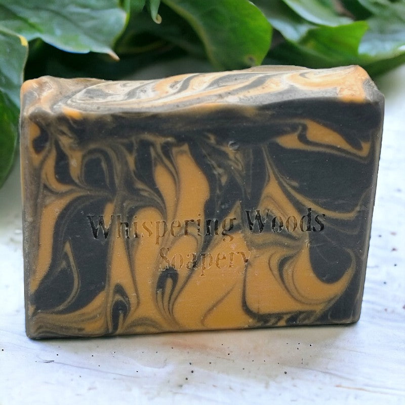 Close-up of one bar of black and orange soap sitting on a white canvas with greenery in the background