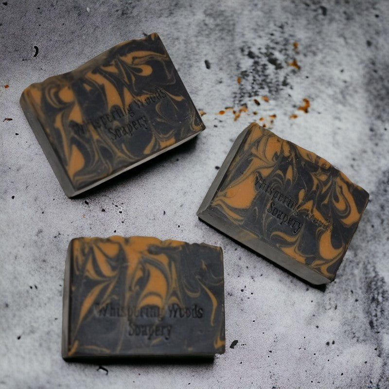 Three bars of black and orange swirled soap laying on their sides on a concrete background