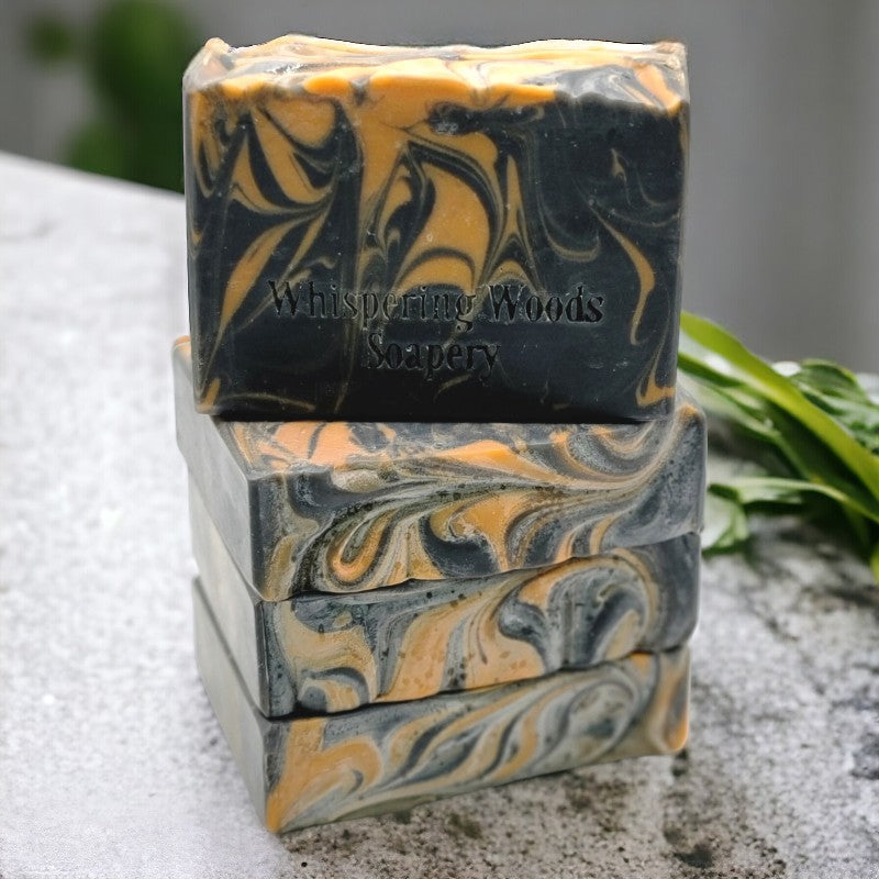 Four bars of black and orange swirled soap set on top of each other, on a concrete counter with plants in the background