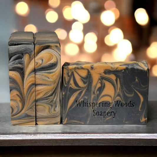 Three bars of black and orange swirled soap, with warm lights in the background