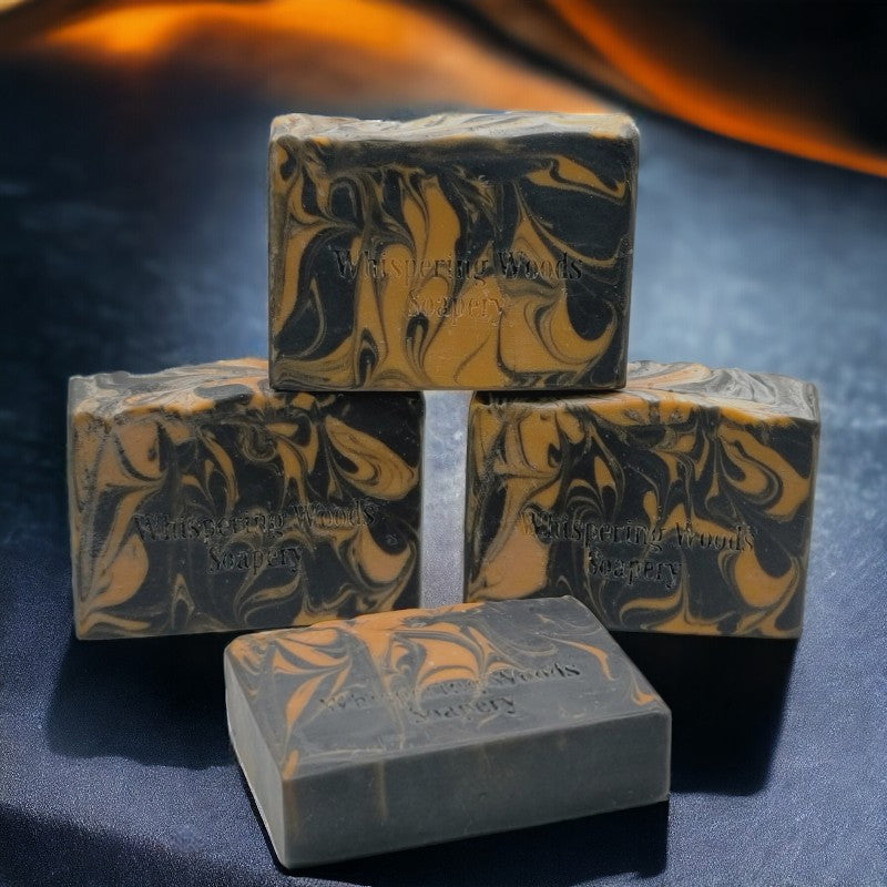 Four bars of black and orange swirled soap on black canvas with orange lights behind them