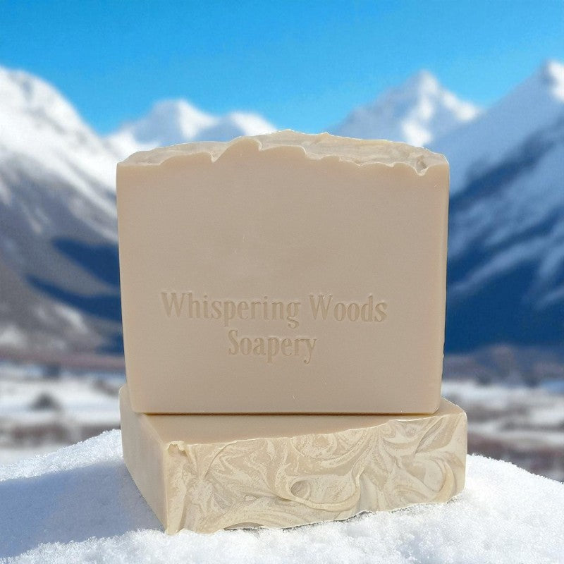 Bars of light tan soap with 'Whispering Woods Soapery' branding on a snowy background with mountains