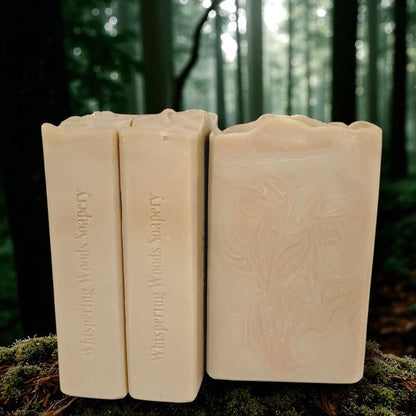 Three bars of creamy tan soap with coppery swirls placed on a forest floor. The bars are stamped Whispering Woods Soapery.