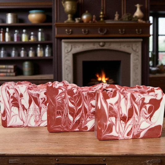 Three bars of red and white marbled soap on a wooden surface with a fireplace in the background